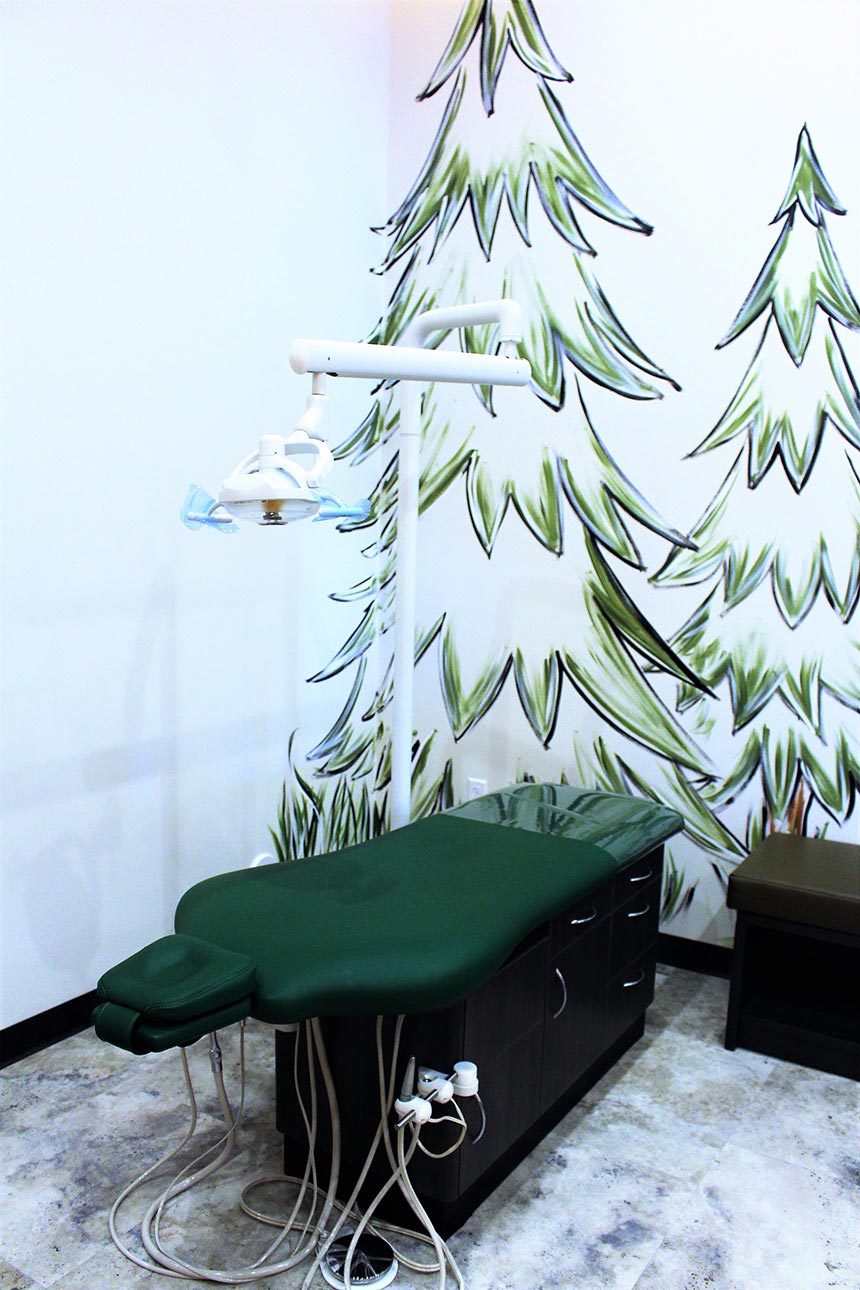The image shows a dental office interior with a mural of Christmas trees on the wall behind a dental chair.