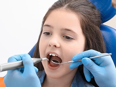 Girl receiving dental care with dentist s help, wearing blue gloves and using dental tools.