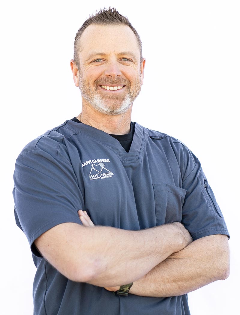 The image shows a man wearing a white coat and standing with his arms crossed, smiling at the camera.