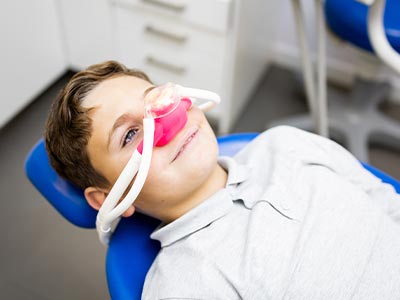 The image depicts a person sitting in a dental chair with a red mouthpiece inserted, wearing glasses, looking directly at the camera, in an indoor setting with a dental office ambiance.