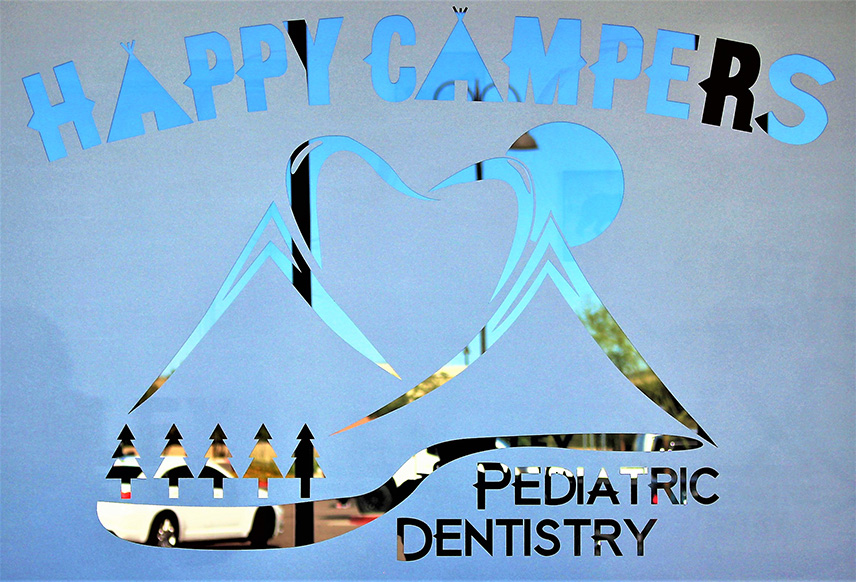 The image shows a sign with the text  Happy Campers  at the top, followed by a stylized graphic of a mountain peak with trees and a blue sky background. Below this graphic are two smaller images  one on the left depicts a pine tree and the other on the right is a graphic of a mountain peak with clouds. The sign also includes text that reads  Pediatric Dentistry  at the bottom, indicating the name of the dental practice.