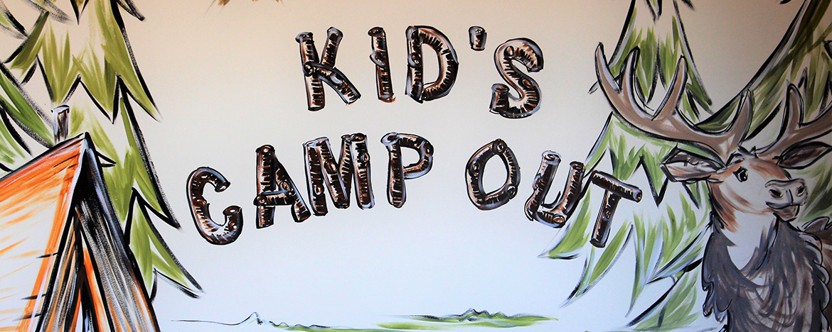 The image shows a sign with text that reads 'Kid's Campout' accompanied by an illustration of a campsite scene, including tents and a forest background.