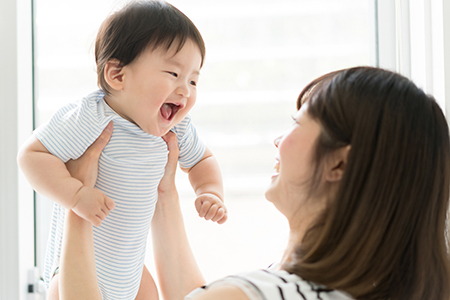 A woman holding a baby while smiling at something off-camera.