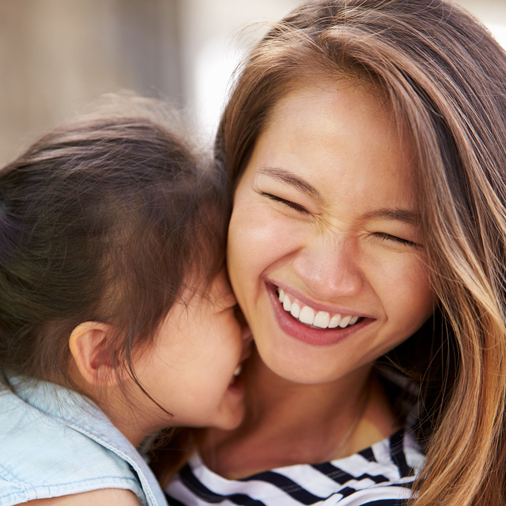 The image shows a woman with a young child, both smiling, sharing an affectionate moment.